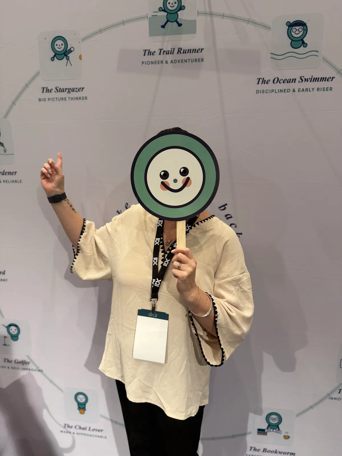 A delegate holding a Heart Bridge Health smiley face sign in front of the founder personas wall