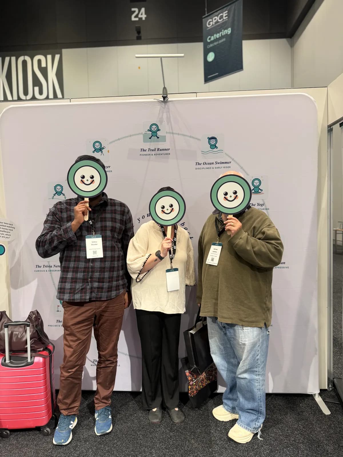 Three conference delegates holding Heart Bridge Health smiley face signs