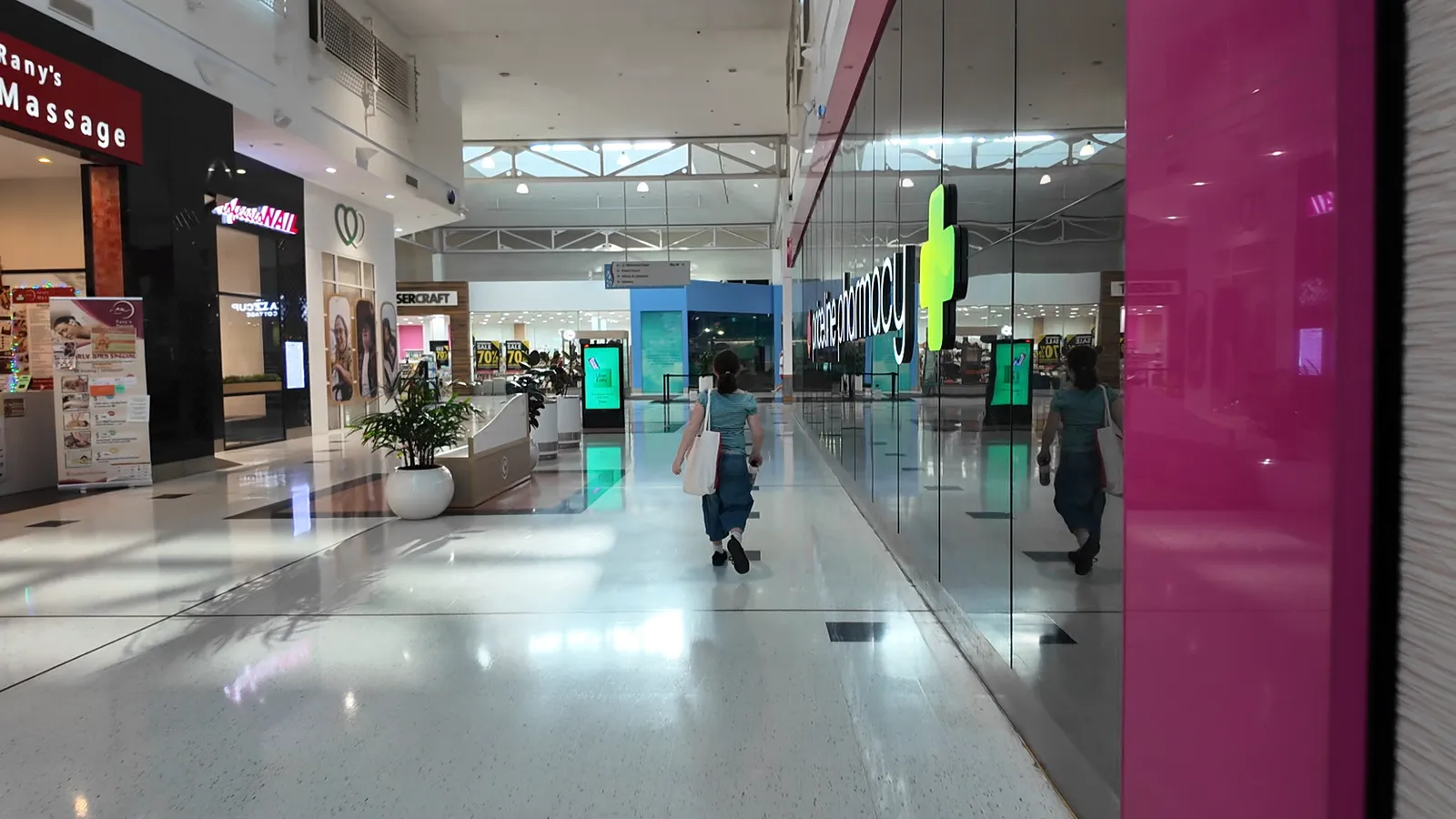 A bright, busy shopping centre walkway with shoppers walking past the shopfronts