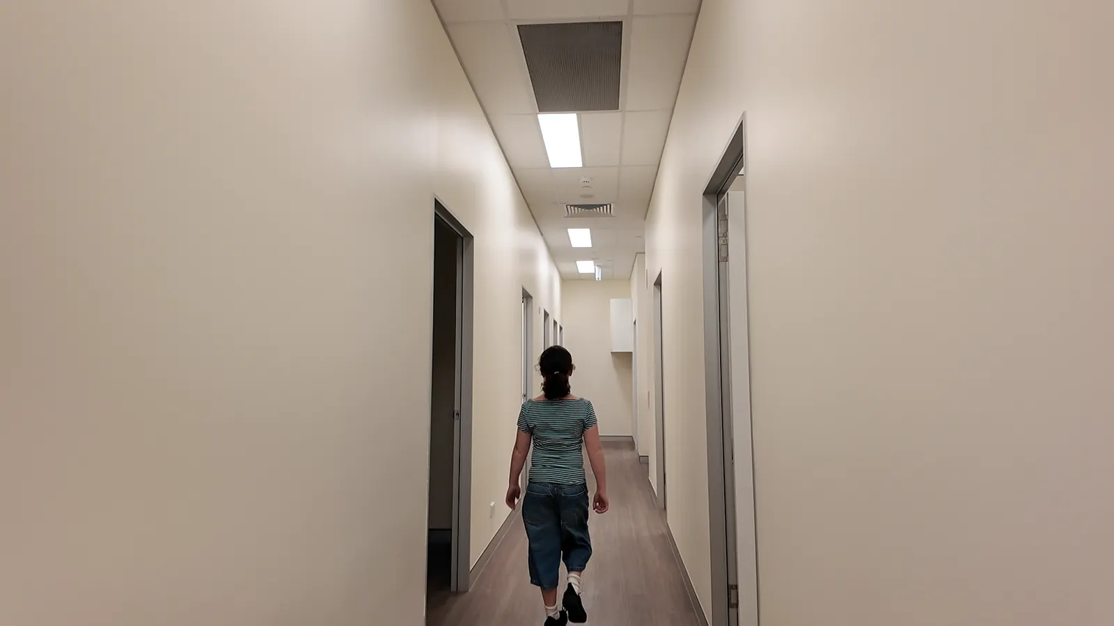 A long, bright, brand new clinic corridor with consulting room doors on either side and a girl walking away down it