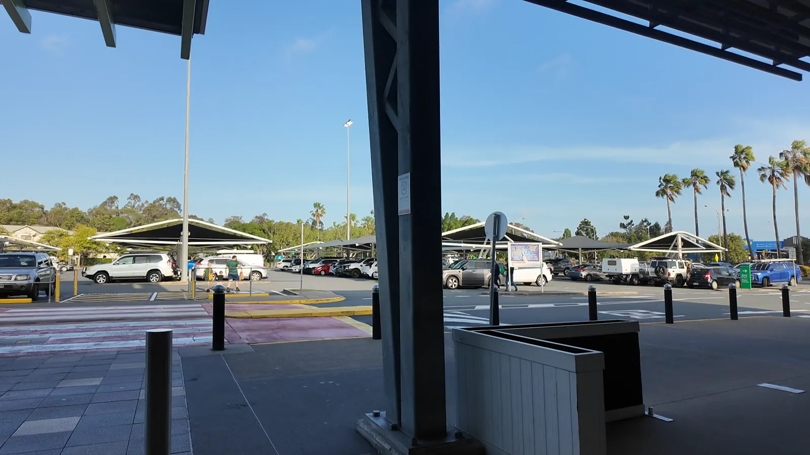 An open-air shopping centre car park lined with palm trees on a sunny afternoon
