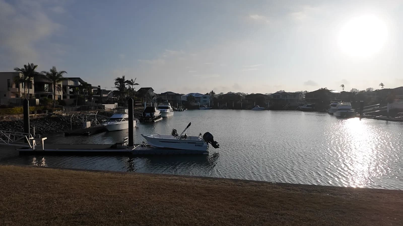 Boats moored along the still water of a Raby Bay canal at sunset, with waterfront homes and palm trees behind
