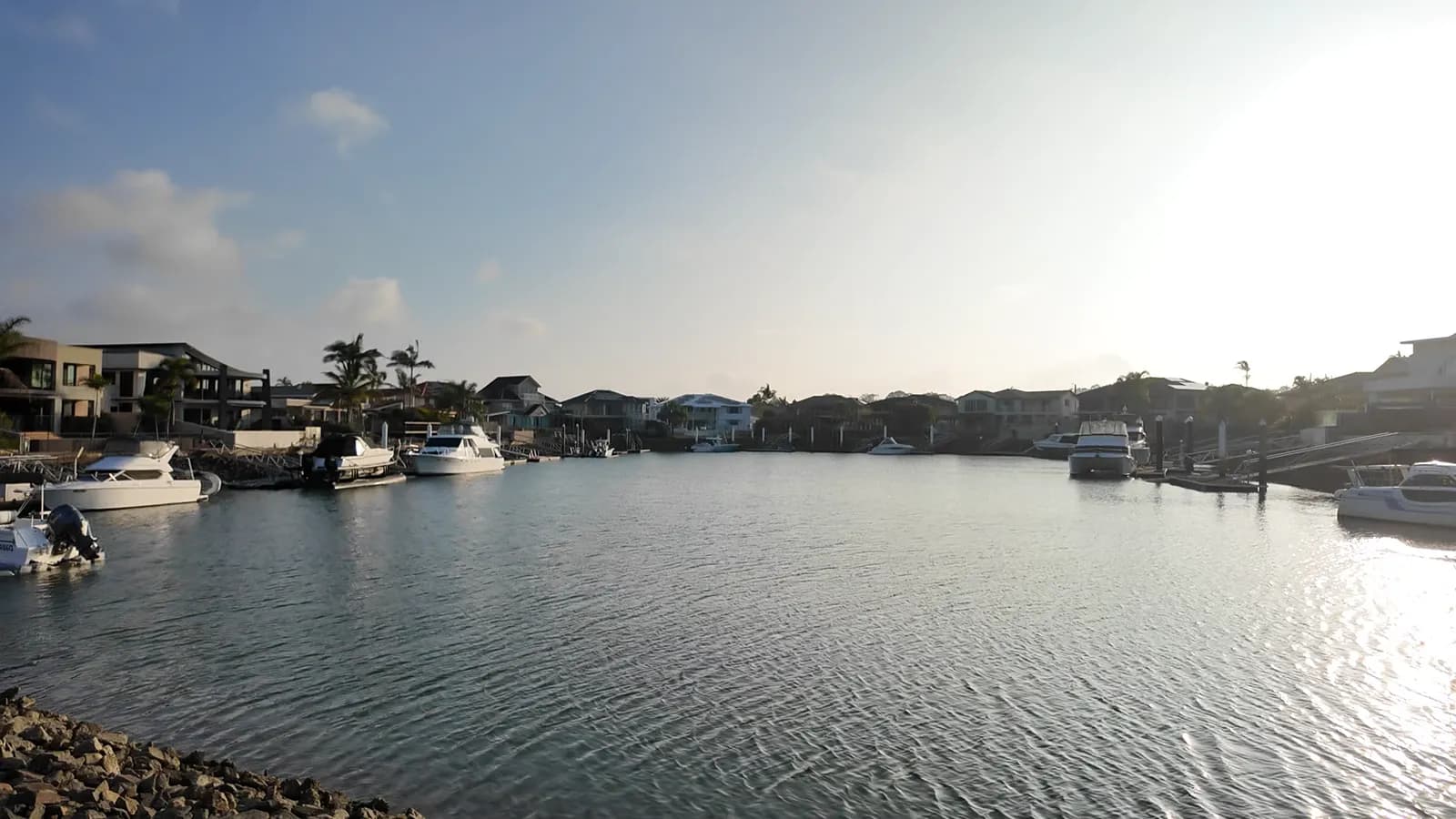 A Raby Bay canal at golden hour, boats moored along the rock wall and waterfront homes across the water