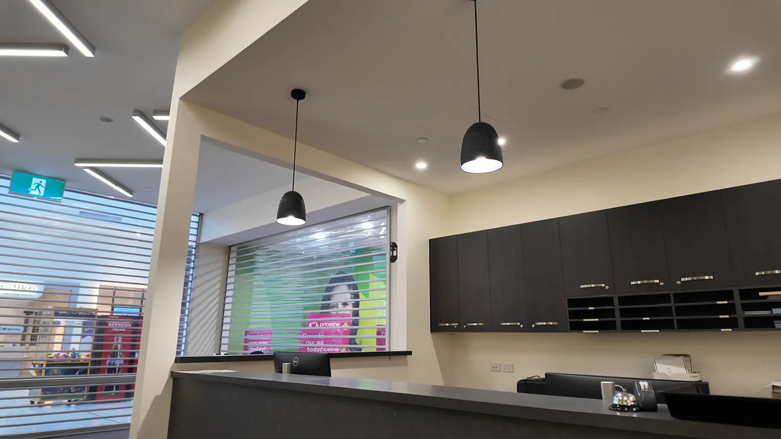 The reception desk of a brand new clinic, with dark timber cabinetry and pendant lights, opening onto a shopping centre walkway