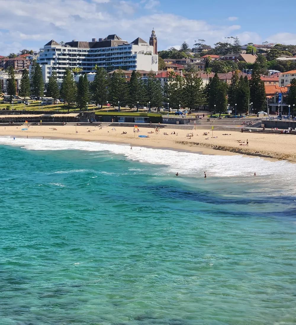Coogee Beach on a clear day, the crescent of sand curving below the apartment blocks and Norfolk Island pines of the suburb behind