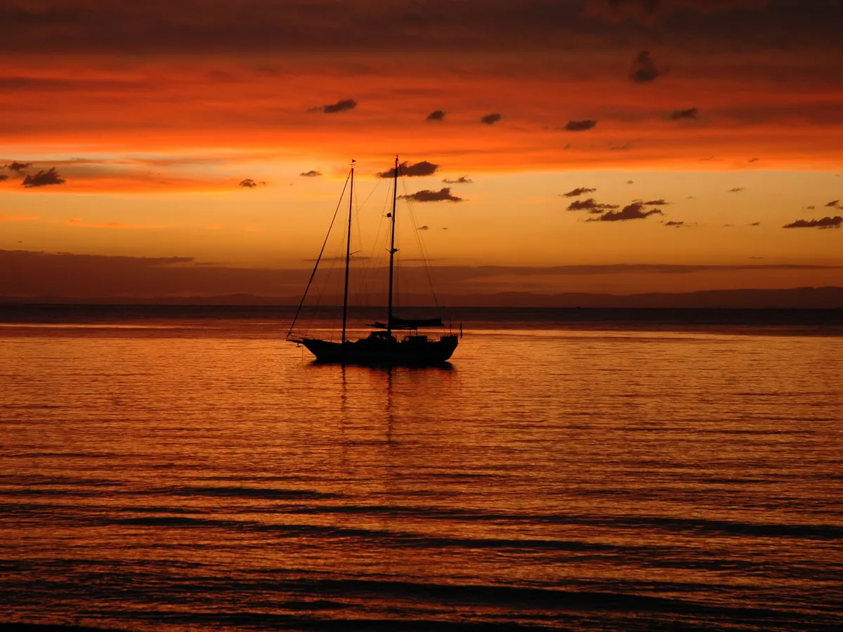 A yacht silhouetted against a deep orange sunset over the calm water of Moreton Bay
