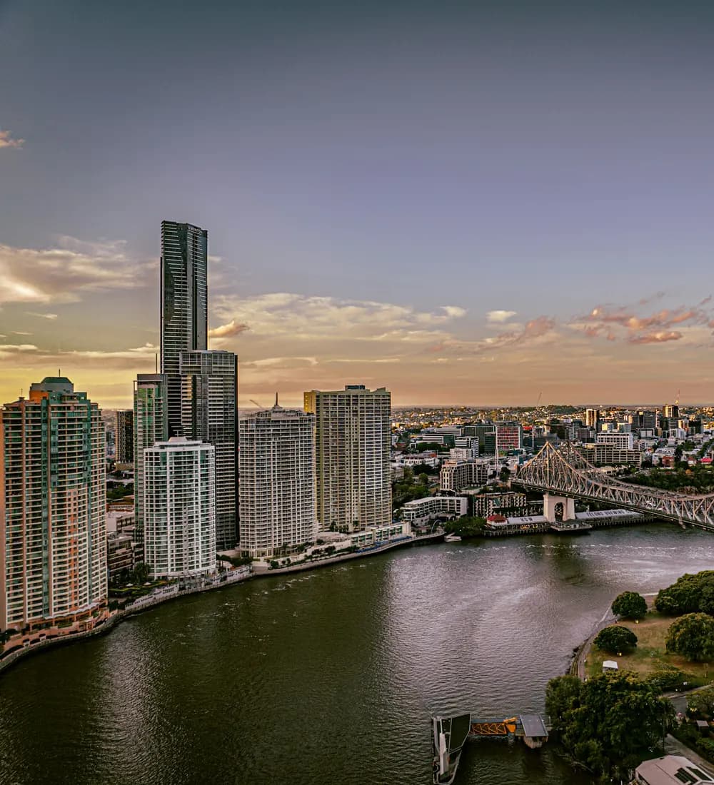 The Brisbane River curving past the city towers at dusk, with the Story Bridge crossing towards the inner-eastern suburbs