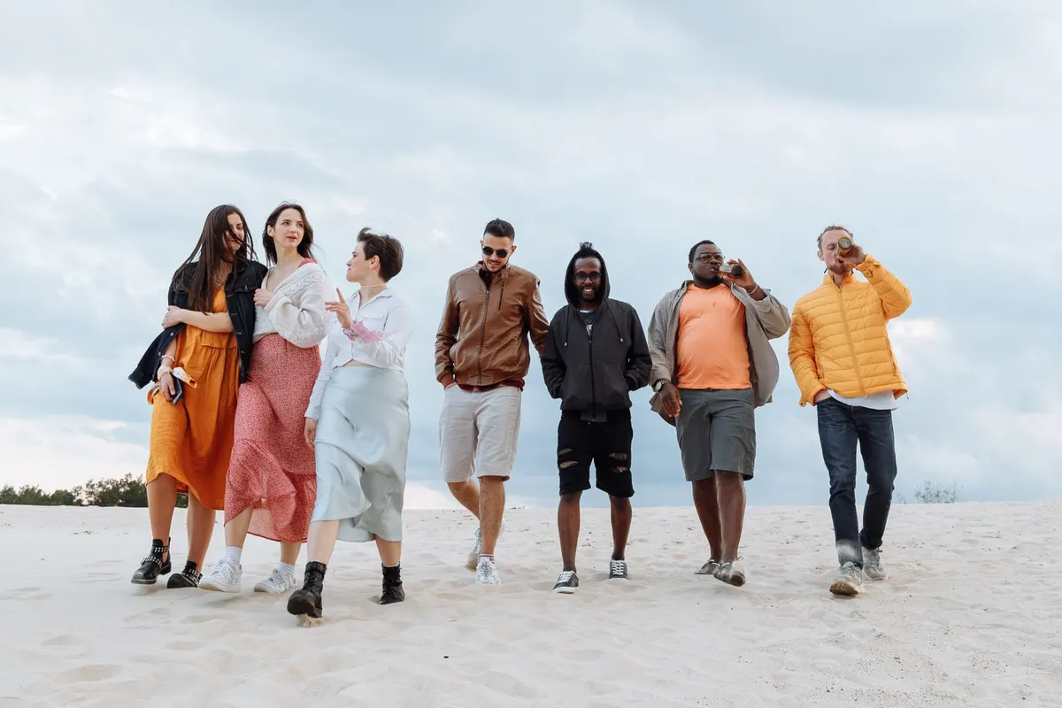 A group of six friends of different backgrounds walking together along a beach, talking and laughing