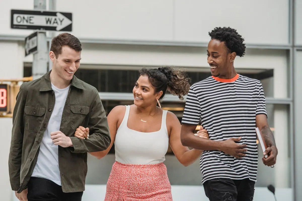 Three friends walking side by side down a city street, mid-conversation and grinning