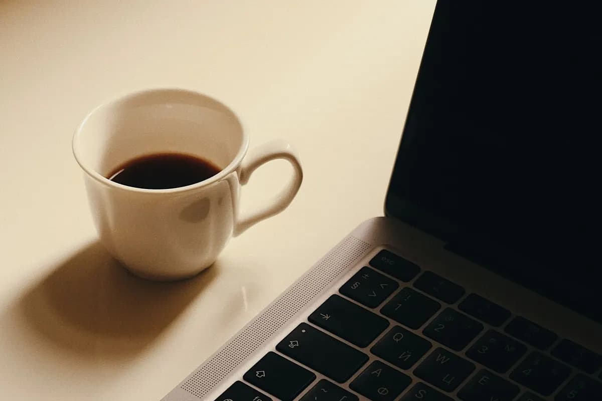 A laptop and a cup of coffee on a desk in warm afternoon light