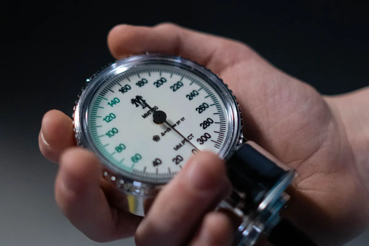 A hand holding the dial of an analogue blood pressure cuff, needle mid-reading