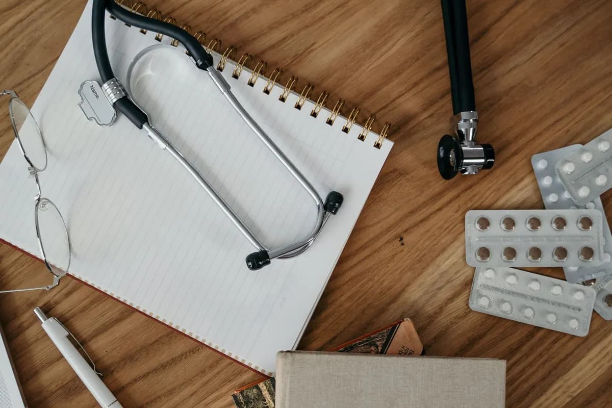 A stethoscope, notebook and glasses laid out on a wooden desk