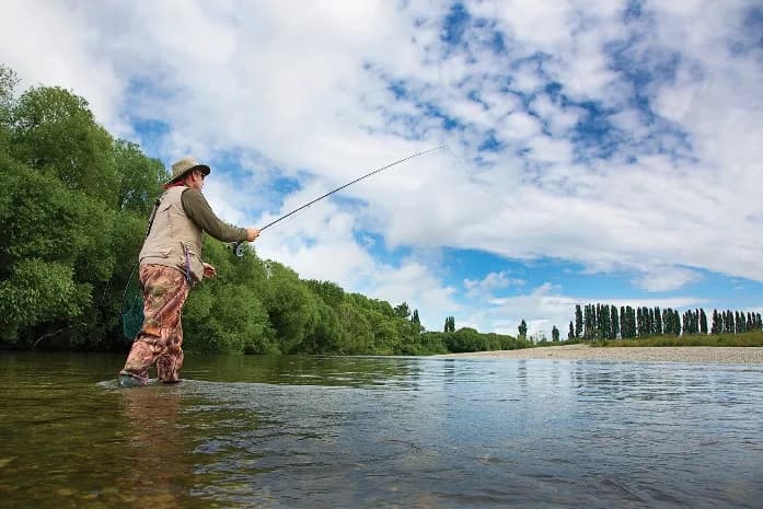 A fly fisher casting into a clear Southland river on a bright day