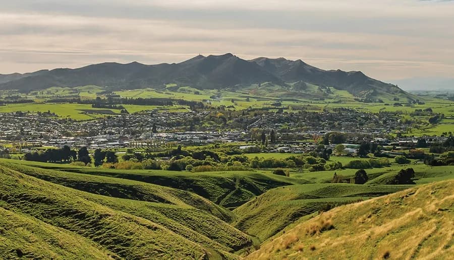 A green Southland valley of farmland and rolling hills below distant ranges